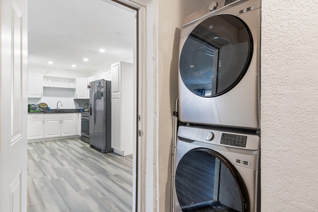 clothes washing area with stacked washer / drying machine and light wood-type flooring