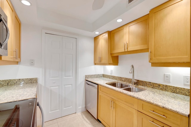 kitchen with stainless steel appliances, light stone counters, light brown cabinetry, sink, and light tile floors