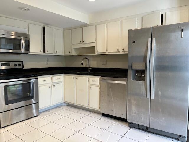 kitchen with white cabinets, appliances with stainless steel finishes, sink, and light tile floors