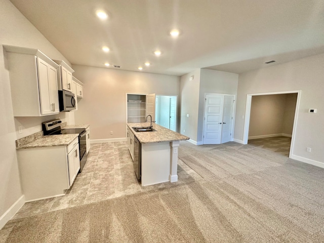 kitchen with light stone countertops, white cabinetry, stainless steel appliances, an island with sink, and light colored carpet