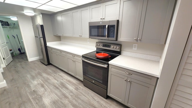 kitchen with appliances with stainless steel finishes, gray cabinetry, and light hardwood / wood-style flooring