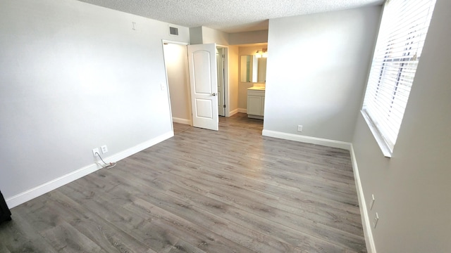 unfurnished bedroom with hardwood / wood-style floors, connected bathroom, and a textured ceiling