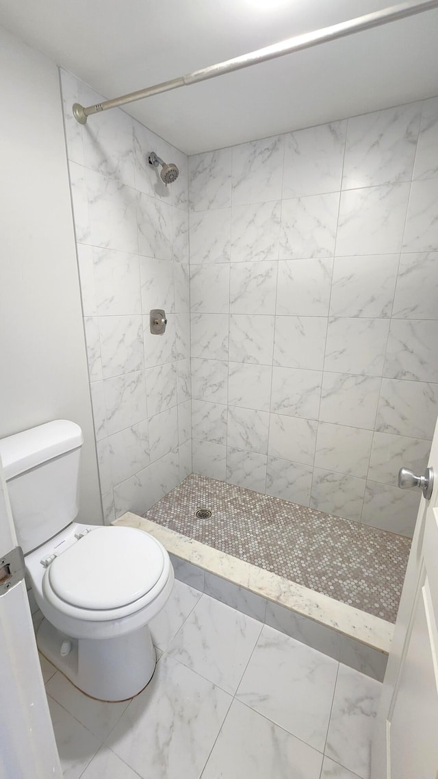 bathroom featuring toilet, tile flooring, and tiled shower