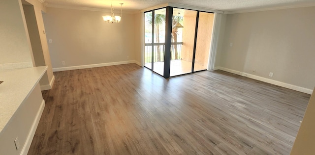 empty room featuring a healthy amount of sunlight, a textured ceiling, wood-type flooring, and an inviting chandelier