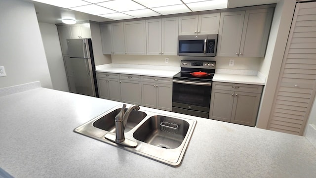 kitchen with a drop ceiling, stainless steel appliances, sink, and gray cabinets