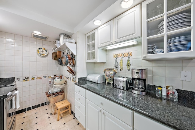 kitchen featuring stainless steel range oven, white cabinetry, tile walls, and dark stone counters