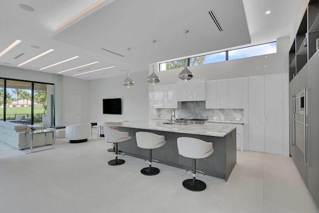 kitchen with a breakfast bar, a wealth of natural light, white cabinetry, backsplash, and hanging light fixtures