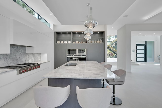 kitchen featuring light stone countertops, hanging light fixtures, backsplash, stainless steel gas stovetop, and sink