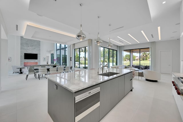 kitchen featuring light tile floors, decorative light fixtures, light stone countertops, a kitchen island with sink, and sink