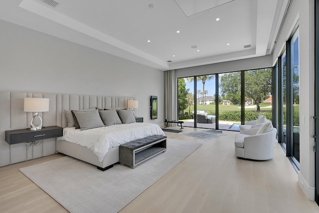 bedroom with a raised ceiling, access to outside, and light wood-type flooring