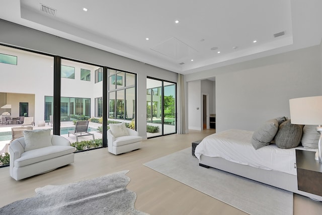 bedroom featuring light wood-type flooring, access to exterior, and a raised ceiling