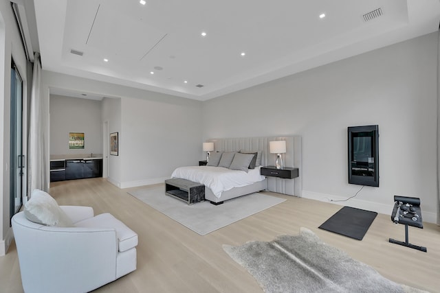 bedroom with a raised ceiling and light wood-type flooring