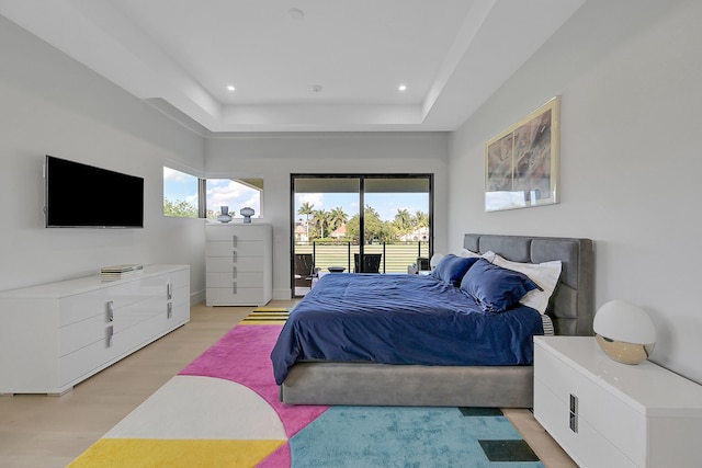 bedroom featuring access to exterior, light wood-type flooring, and a tray ceiling