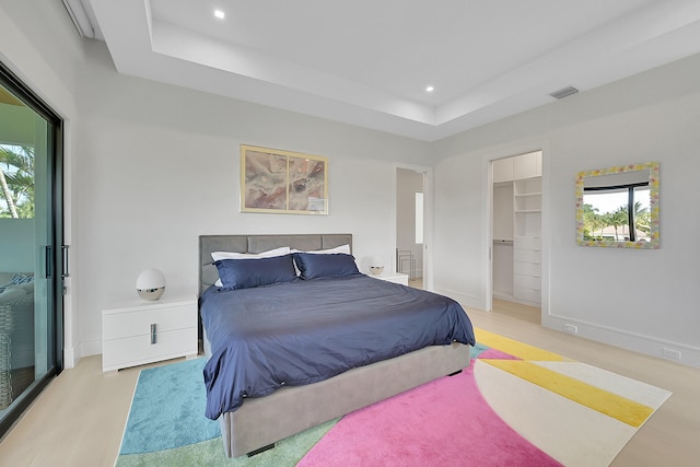 bedroom with a walk in closet, multiple windows, and light hardwood / wood-style flooring