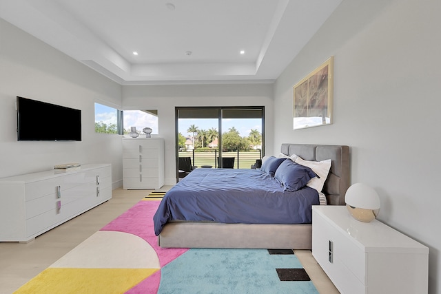 bedroom with access to outside, a tray ceiling, and light hardwood / wood-style floors