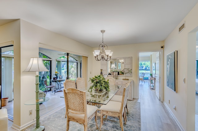 dining space with light hardwood / wood-style floors, ceiling fan with notable chandelier, and a healthy amount of sunlight