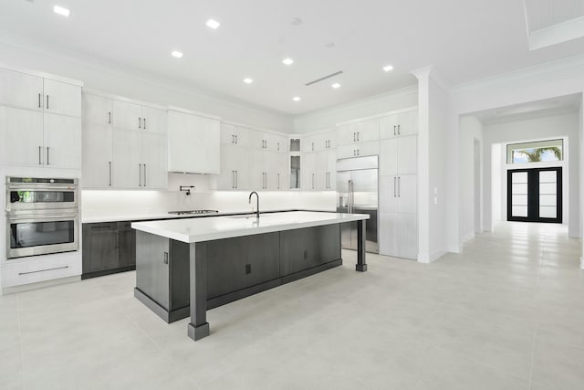 kitchen with white cabinetry, a breakfast bar area, a kitchen island with sink, appliances with stainless steel finishes, and ornamental molding