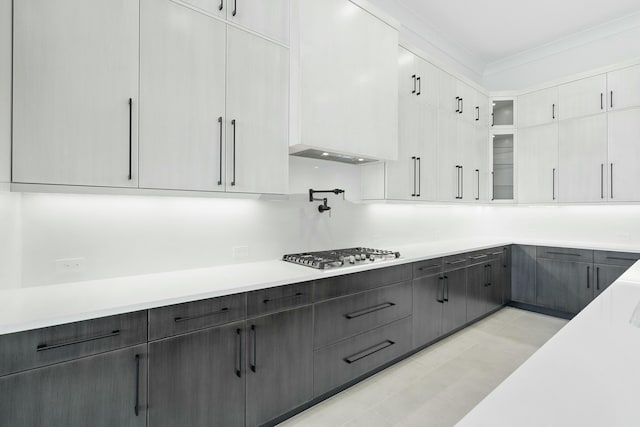 kitchen featuring light tile patterned floors, white cabinetry, stainless steel gas stovetop, and crown molding