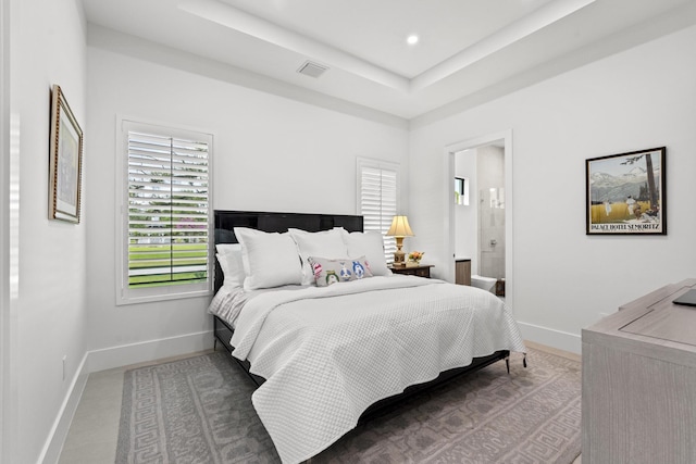 bedroom with connected bathroom, a tray ceiling, and multiple windows