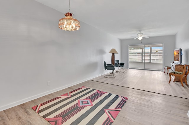 sitting room with light wood-type flooring and ceiling fan with notable chandelier