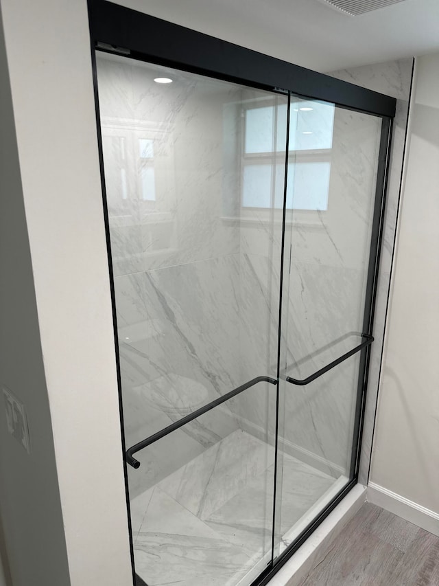 full bath featuring baseboards, a marble finish shower, and wood finished floors