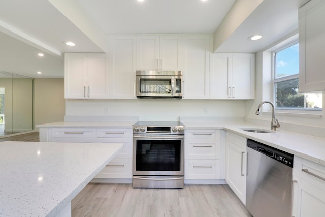 kitchen featuring light stone counters, white cabinetry, stainless steel appliances, and a sink