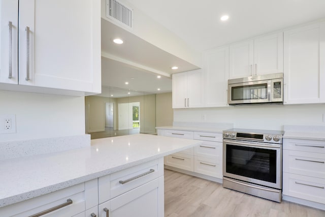 kitchen featuring light stone counters, visible vents, white cabinetry, appliances with stainless steel finishes, and light wood finished floors