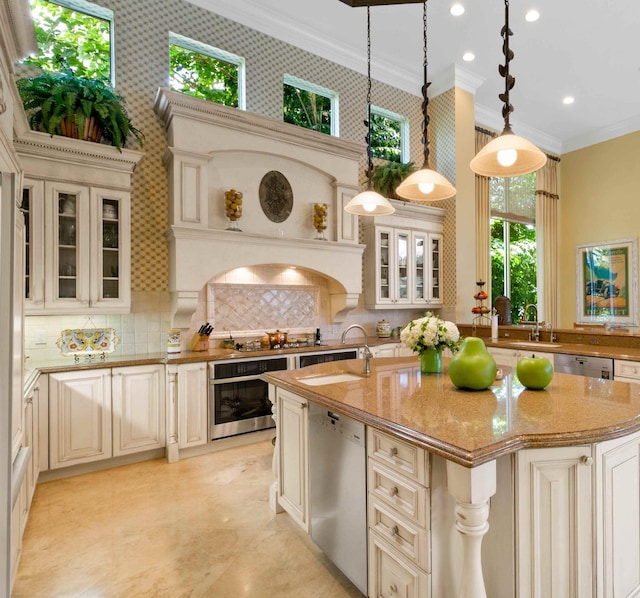 kitchen with light stone counters, appliances with stainless steel finishes, tasteful backsplash, decorative light fixtures, and a center island with sink