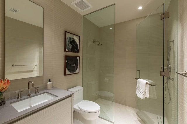 bathroom with vanity, a shower with shower door, toilet, and tile walls