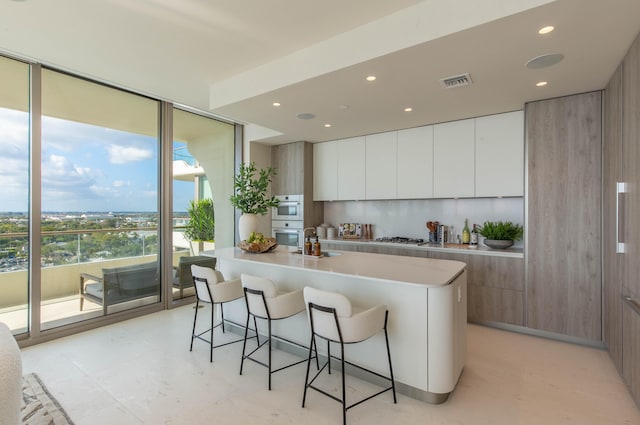 kitchen with an island with sink, stainless steel gas cooktop, a breakfast bar, tasteful backsplash, and white cabinetry