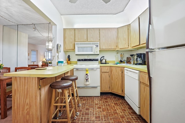 kitchen featuring kitchen peninsula, a textured ceiling, white appliances, sink, and a breakfast bar area