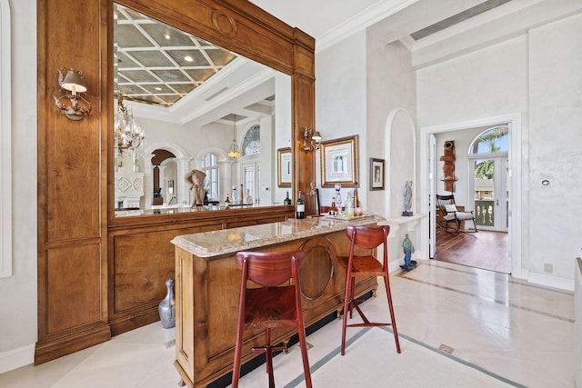 bar featuring light tile floors, a notable chandelier, light stone counters, and ornamental molding