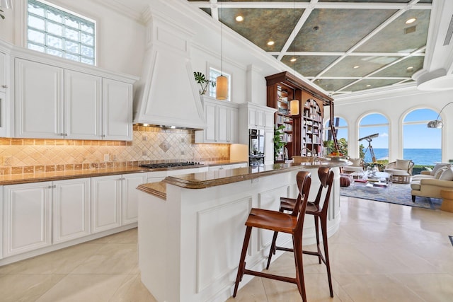 kitchen featuring a breakfast bar, white cabinetry, a water view, custom range hood, and stainless steel gas cooktop