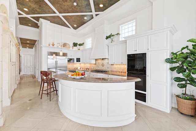 kitchen featuring white cabinets, a center island, a towering ceiling, and built in appliances