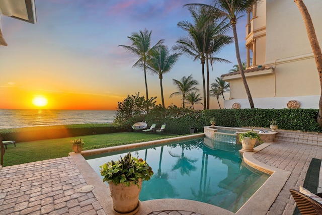 pool at dusk with an in ground hot tub, a water view, and a patio