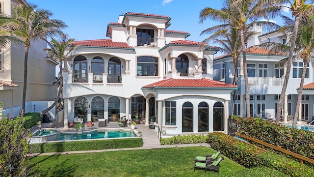 rear view of house with a balcony, a lawn, and french doors