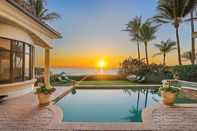 pool at dusk with an in ground hot tub, a patio, and a water view