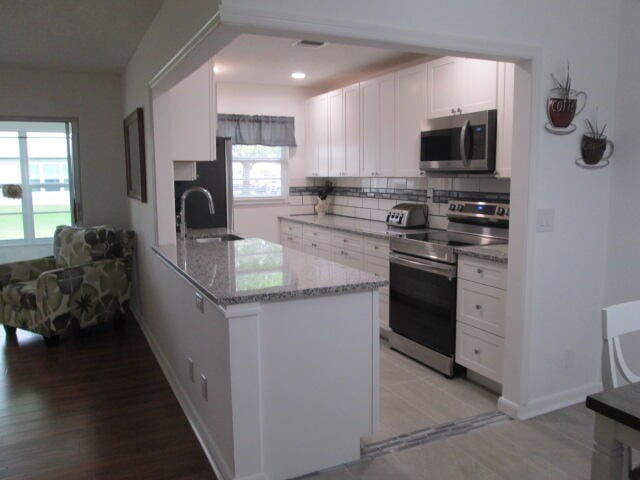 kitchen featuring stainless steel appliances, white cabinetry, sink, and light stone counters