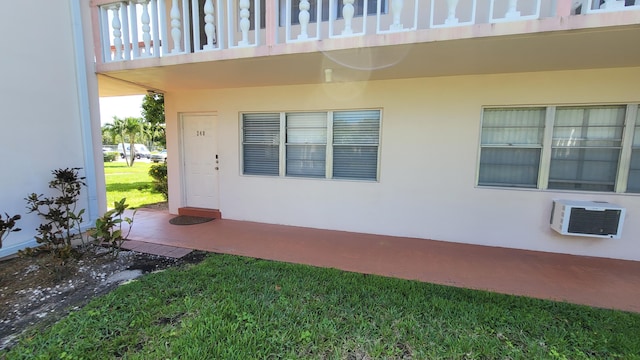 entrance to property featuring a balcony, a lawn, and a wall unit AC