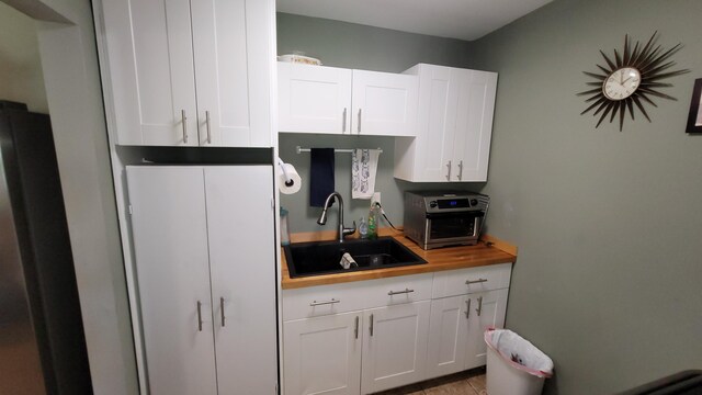 kitchen with wood counters, white cabinets, sink, and refrigerator