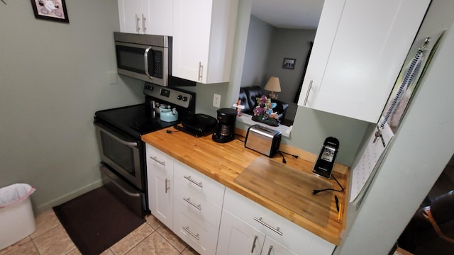 kitchen featuring butcher block counters, light tile flooring, white cabinetry, and range with electric cooktop