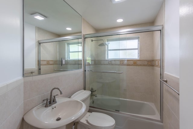 full bathroom featuring sink, shower / bath combination with glass door, toilet, and tile walls