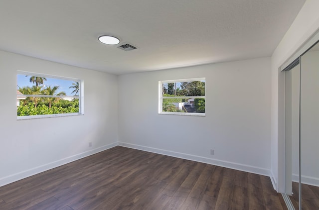 unfurnished bedroom featuring multiple windows, dark wood-type flooring, and a closet