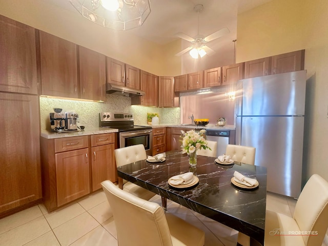 kitchen with light tile patterned floors, ceiling fan, stainless steel appliances, a high ceiling, and backsplash