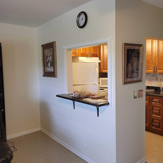 kitchen featuring light tile flooring, backsplash, white fridge, and dark stone countertops