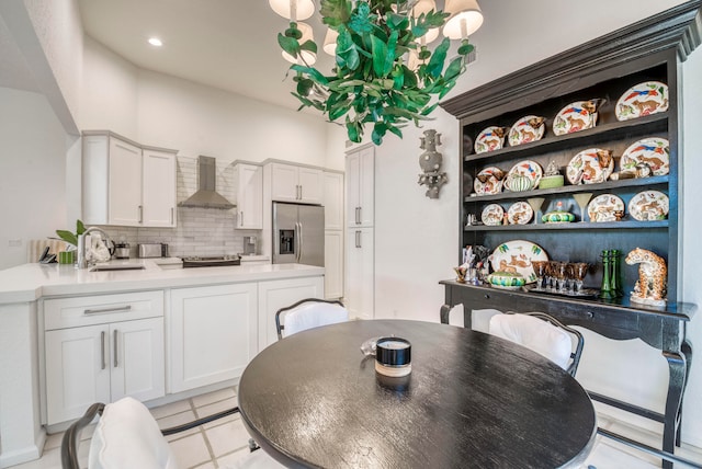 kitchen featuring light tile floors, wall chimney range hood, stainless steel fridge with ice dispenser, tasteful backsplash, and white cabinets