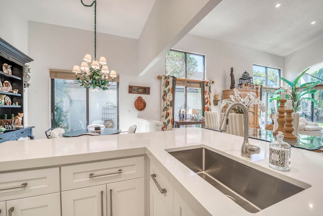 kitchen with white cabinets, a healthy amount of sunlight, a notable chandelier, and sink