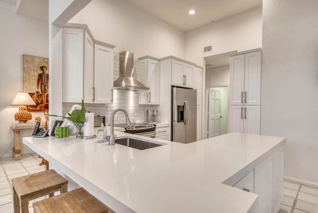 kitchen featuring backsplash, light tile flooring, a kitchen breakfast bar, stainless steel appliances, and wall chimney range hood