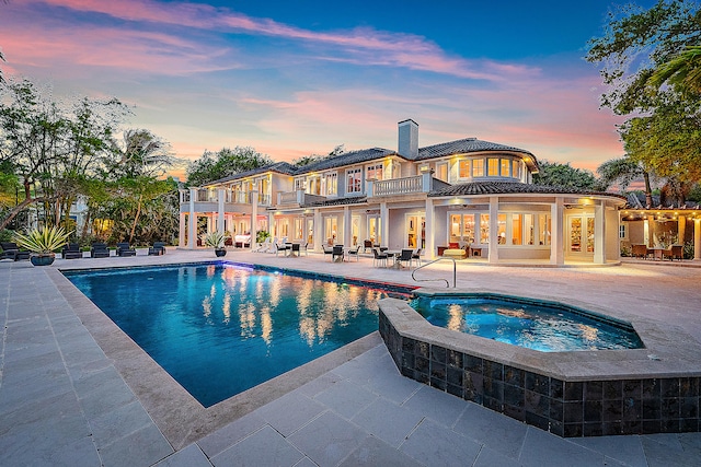 pool at dusk with a patio area and an in ground hot tub