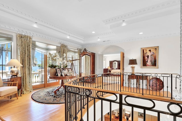 hallway featuring ornamental molding, light hardwood / wood-style floors, and a raised ceiling